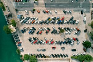 Large parking lot with colorful cars standing in rows on the seashore. Drone
